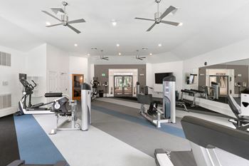 A gym with treadmills and other exercise equipment and ceiling fans
